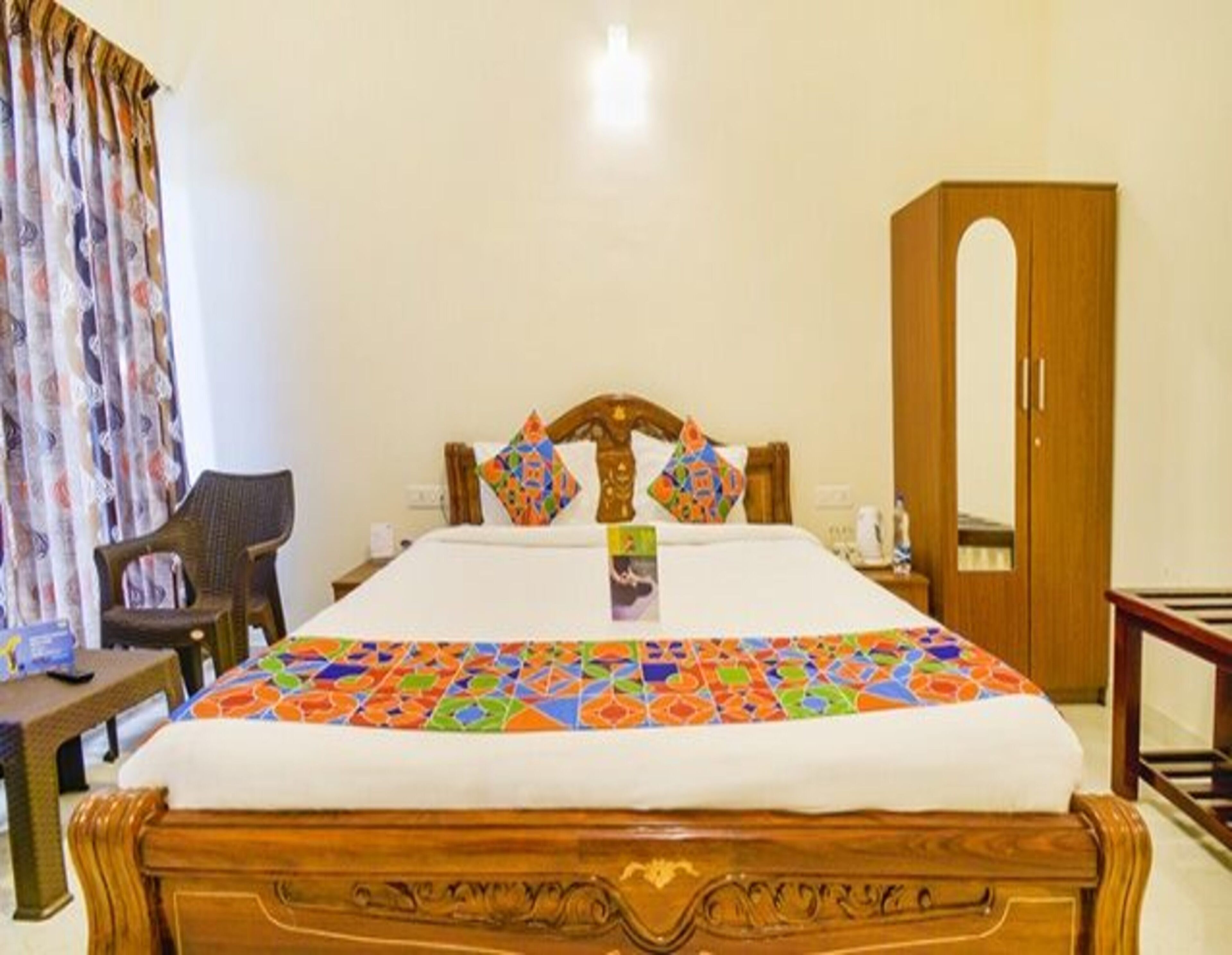 A hotel room with a wooden bed, colorful bedspread, a wooden wardrobe, and a chair.