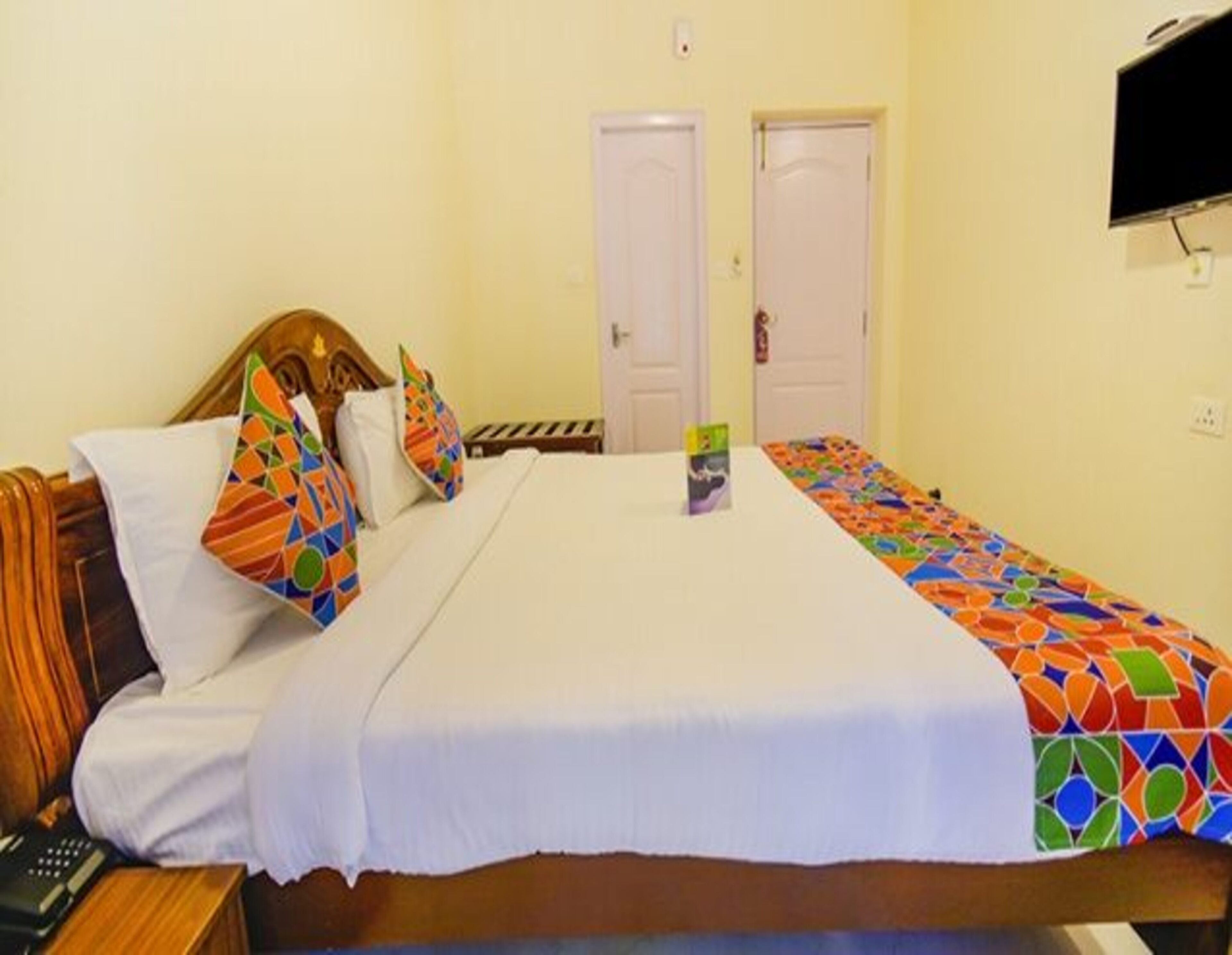 A hotel room with a bed, a nightstand, a television, and two doors.