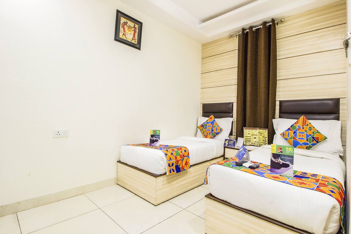 A hotel room with two beds, a wooden headboard, a framed picture on the wall, and a small table with a book and a remote control.