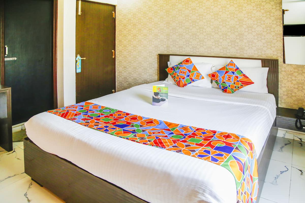 A hotel room with a neatly made bed, a wooden wardrobe, and a patterned wall.