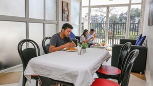 A dining area with a table covered by a white tablecloth, surrounded by black chairs. There are two people dining, and a third person is visible in the background. - FabHotel Eleanora Inn (Barasat)