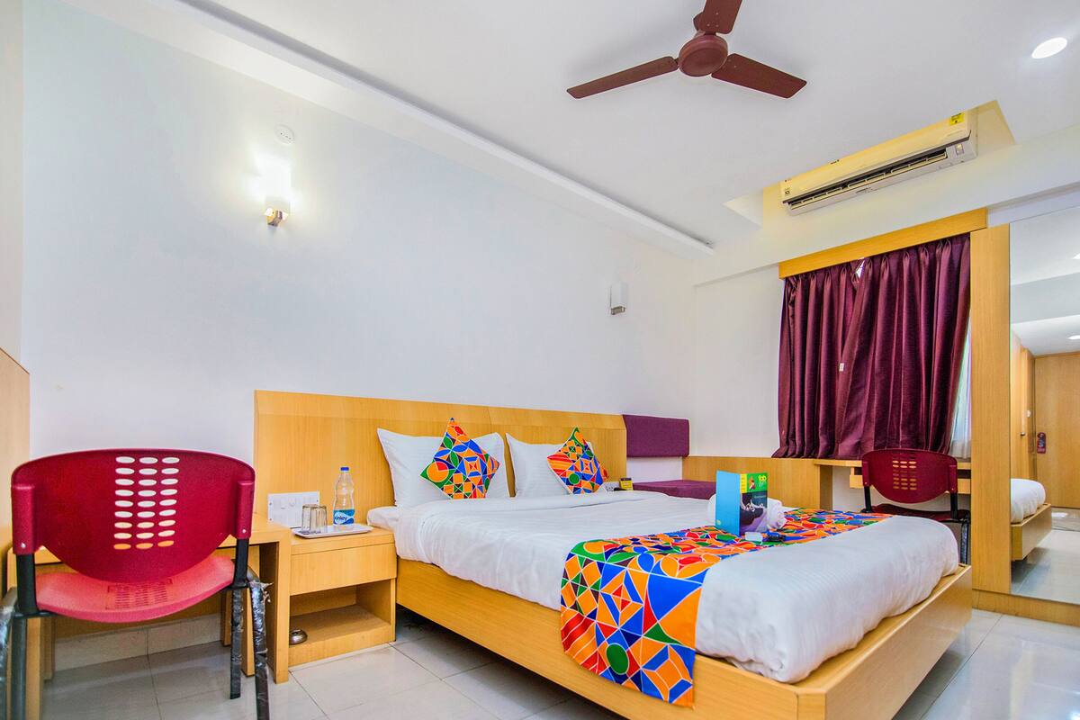 Een hotelkamer met een bed, een bureau, een stoel en een plafondventilator.