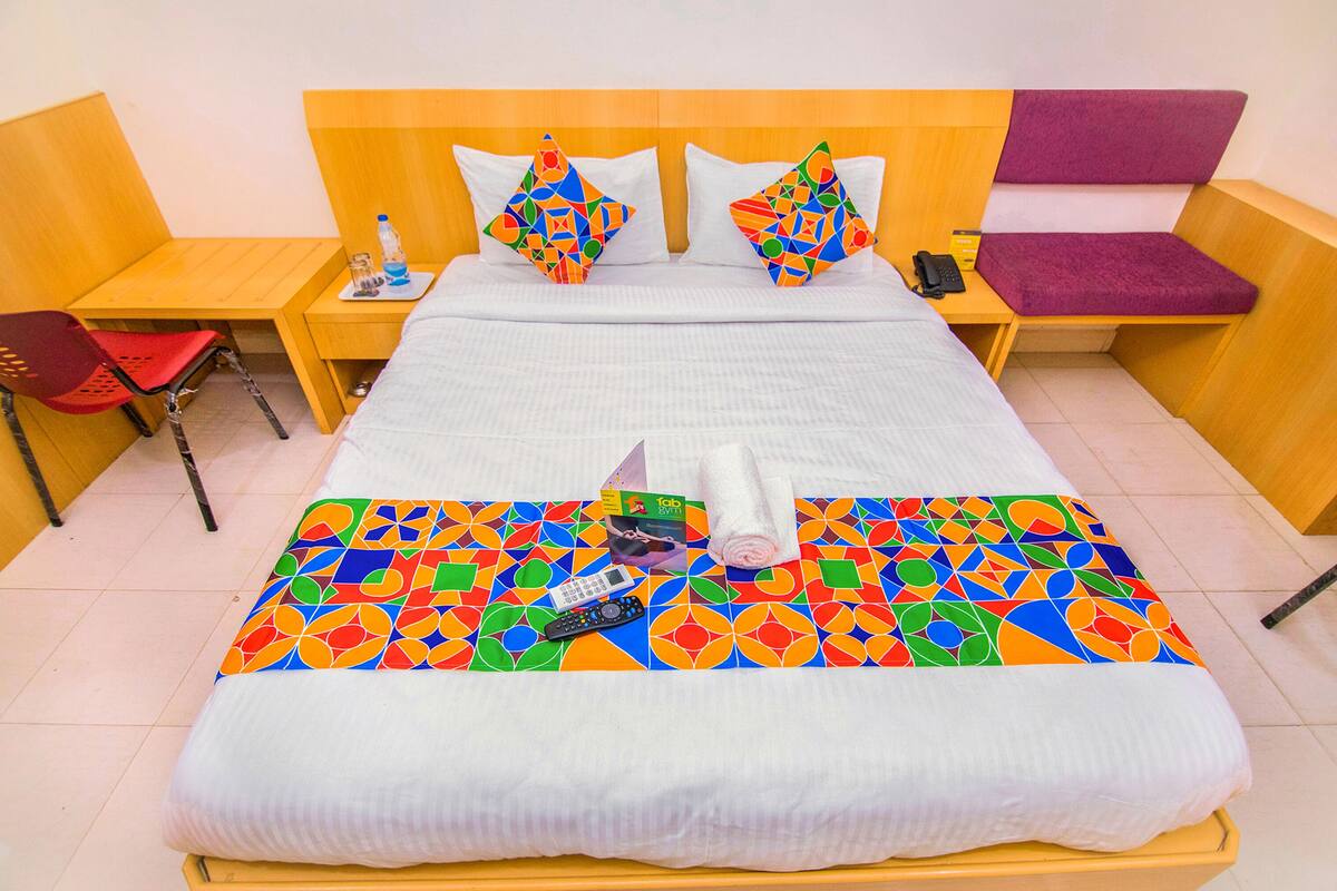 Een hotelkamer met een bed, een houten nachtkastje, een rode stoel en een paarse bank.