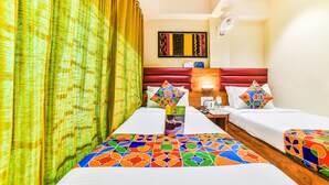 Habitación de hotel con dos camas, cabecera de madera, ventilador de pared y colcha con un estampado geométrico y colorido.