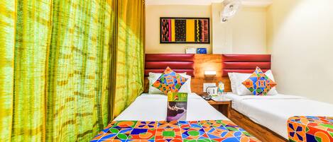 Een hotelkamer met twee bedden, een houten hoofdbord, een ventilator aan de muur en een kleurrijk beddegoed met een geometrisch patroon.