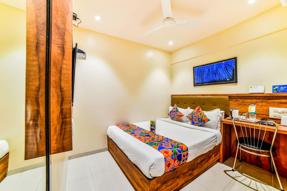 A hotel room with a bed, a desk, a chair, a television, and a ceiling fan.