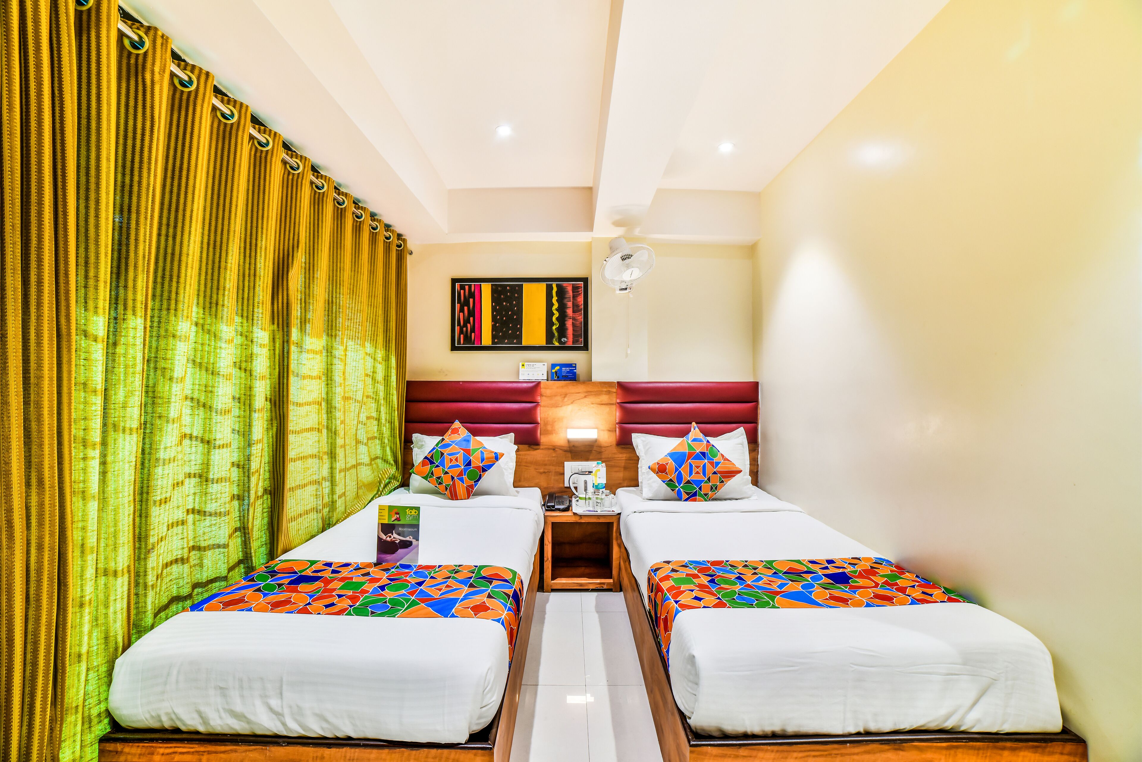 A hotel room with two single beds, a wooden nightstand, a ceiling fan, and a wall-mounted artwork.