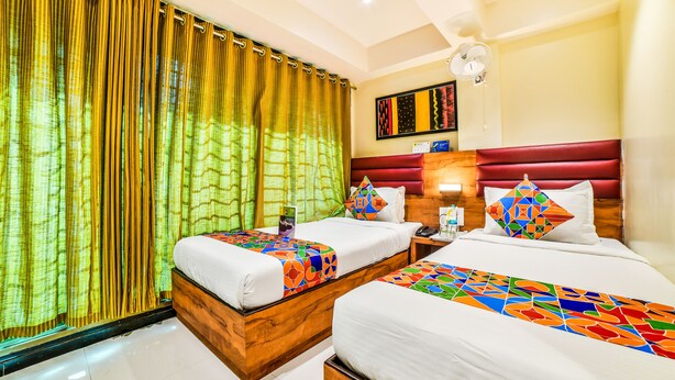 Habitación de hotel con dos camas, cabecero de madera, mesita de noche con lámpara y ventana con cortinas.