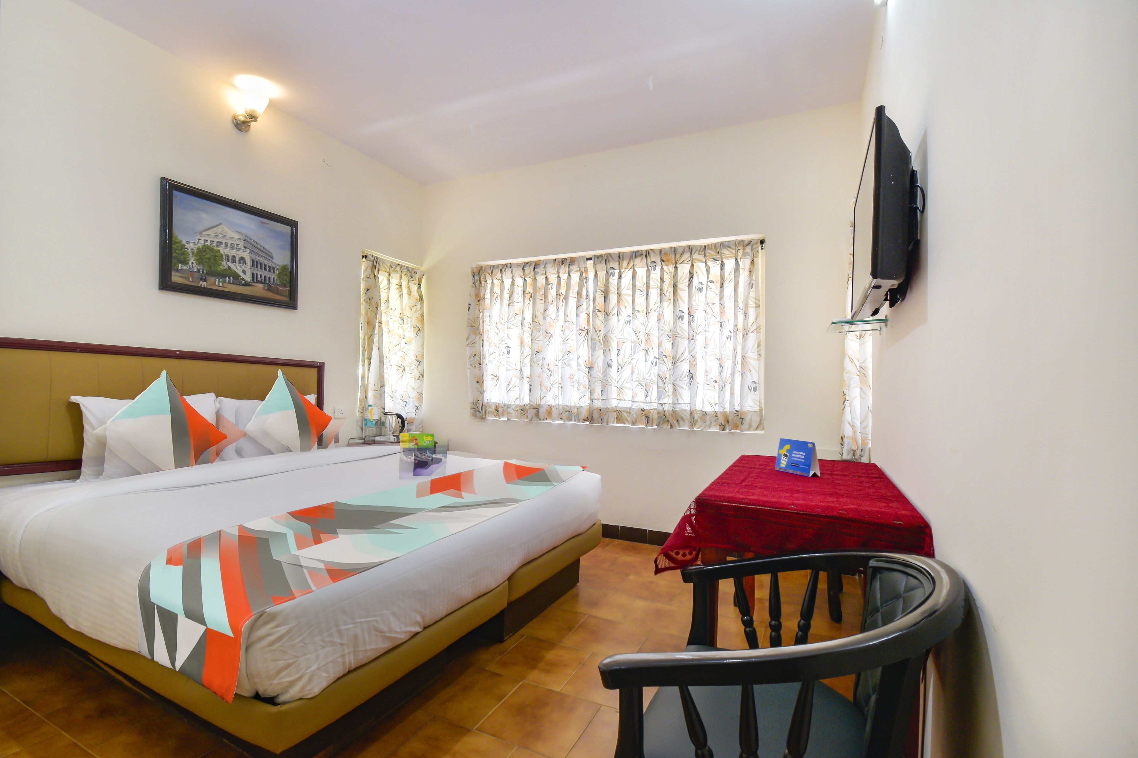 Une chambre d’hôtel avec un lit, un bureau, une chaise, une télévision et une fenêtre avec des rideaux.