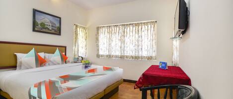 A hotel room with a bed, a desk, a chair, a television, and a window with curtains.