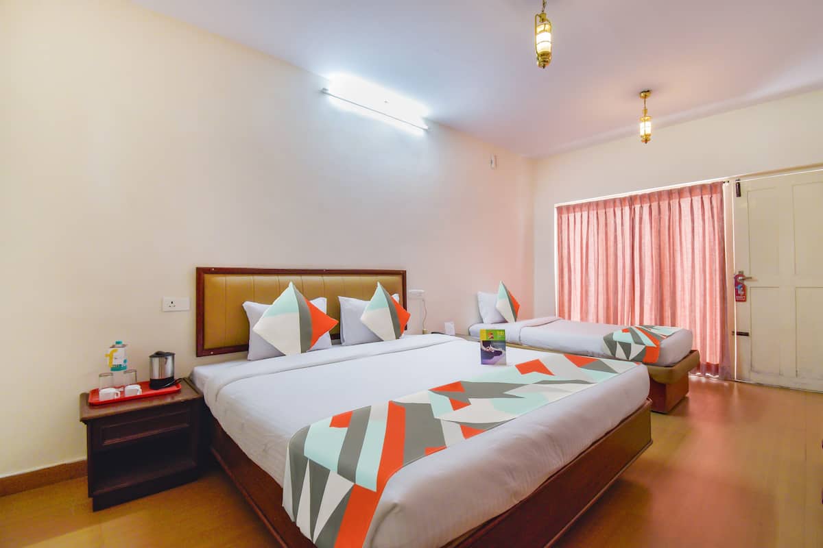 A hotel room with two beds, a nightstand with a tray of breakfast items, a bedside table, and a door with a pink curtain.