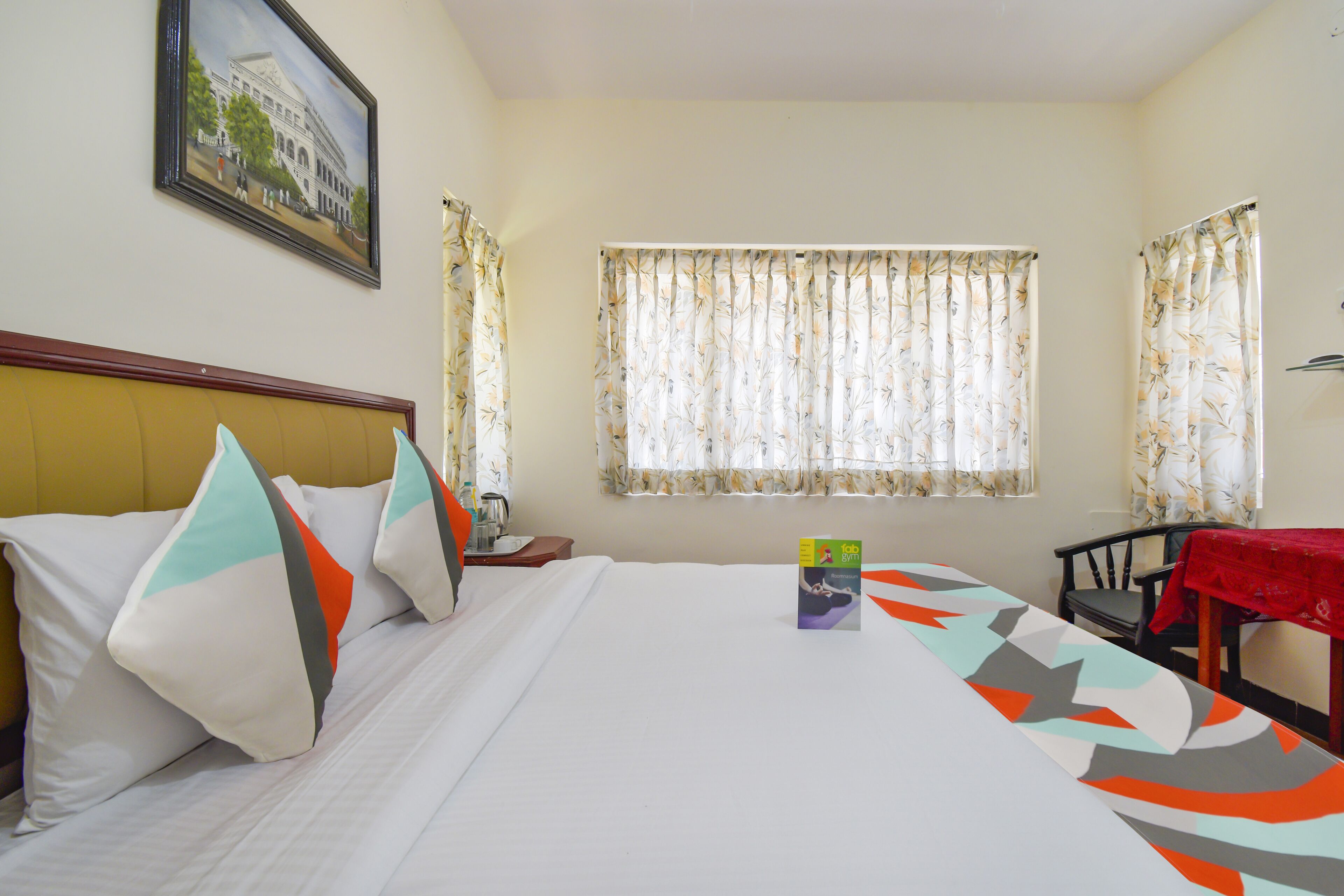 Una habitación de hotel con cama, almohadas, una mesa con mantel rojo y una silla.