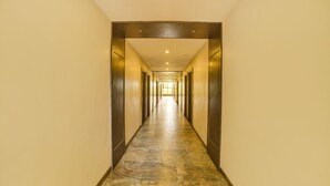 A long, narrow hallway with stone flooring and wooden doors on both sides. - FabHotel Bee Town - AB Road (Indore)
