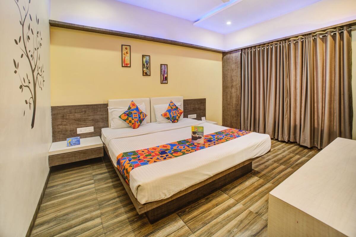 A hotel room with a large bed, wooden flooring, a nightstand, a bedside table, and a window with curtains.