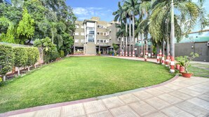 A courtyard with a well-maintained lawn, a tiled walkway, and a building with multiple floors and balconies. - FabHotel Bee Town - AB Road (Indore)