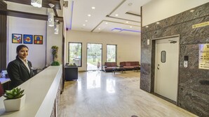 A reception area with a receptionist, a reception desk, a seating area with a sofa, and a door with a sign. - FabHotel Bee Town - AB Road (Indore)