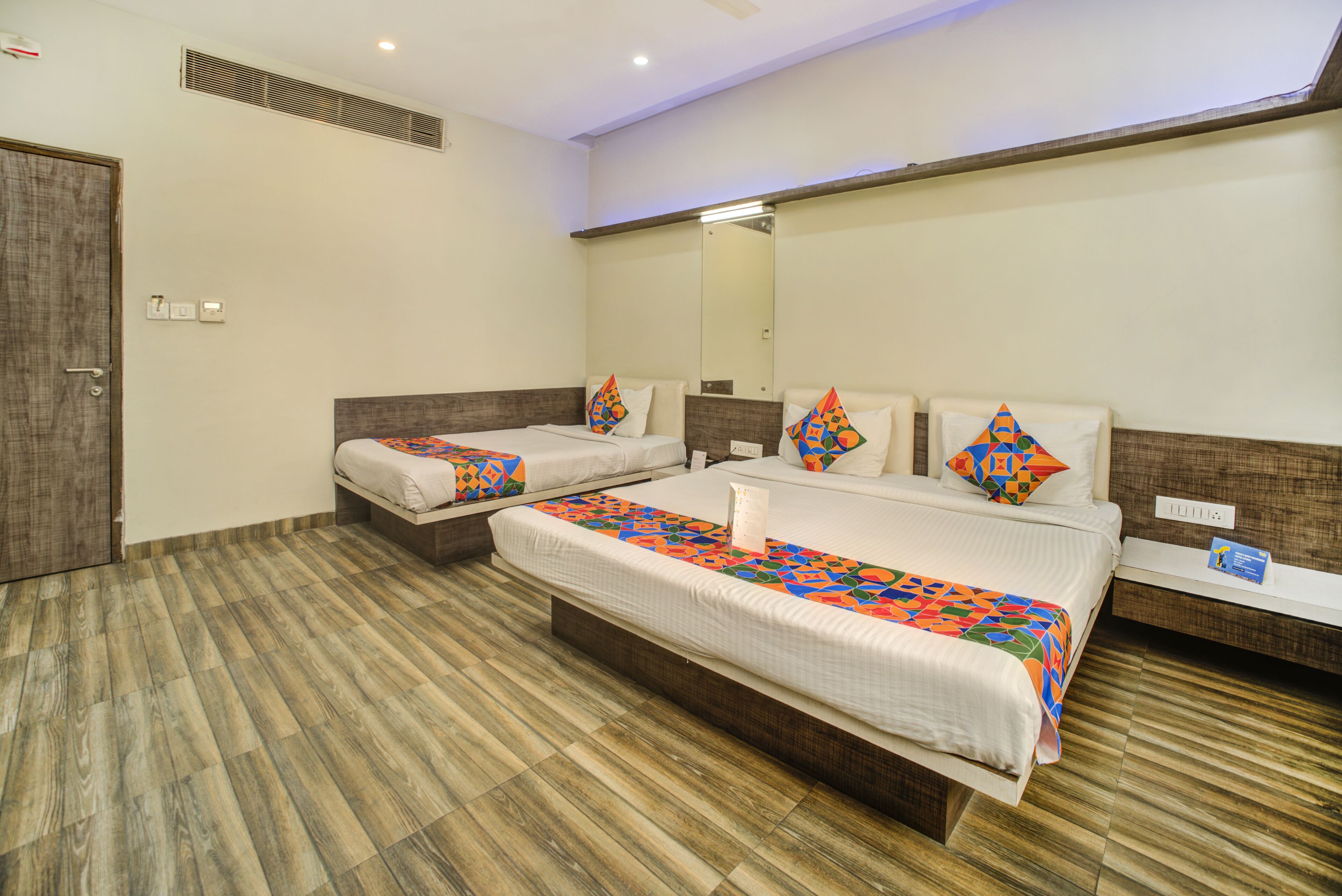 A hotel room with two beds, wooden flooring, and a large mirror on the wall.