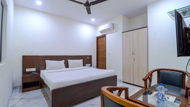 A hotel room with a bed, a nightstand, a desk with a chair, a ceiling fan, an air conditioner, and a wardrobe. - Fabhotel Casa (Mohali)