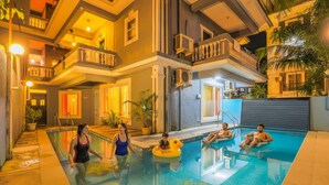 A swimming pool area with a multi-level building, a covered outdoor seating area, and a poolside bar. - Fabhotel Royal Mirage With Pool & Gym - Nr Candolim Beach (Candolim)