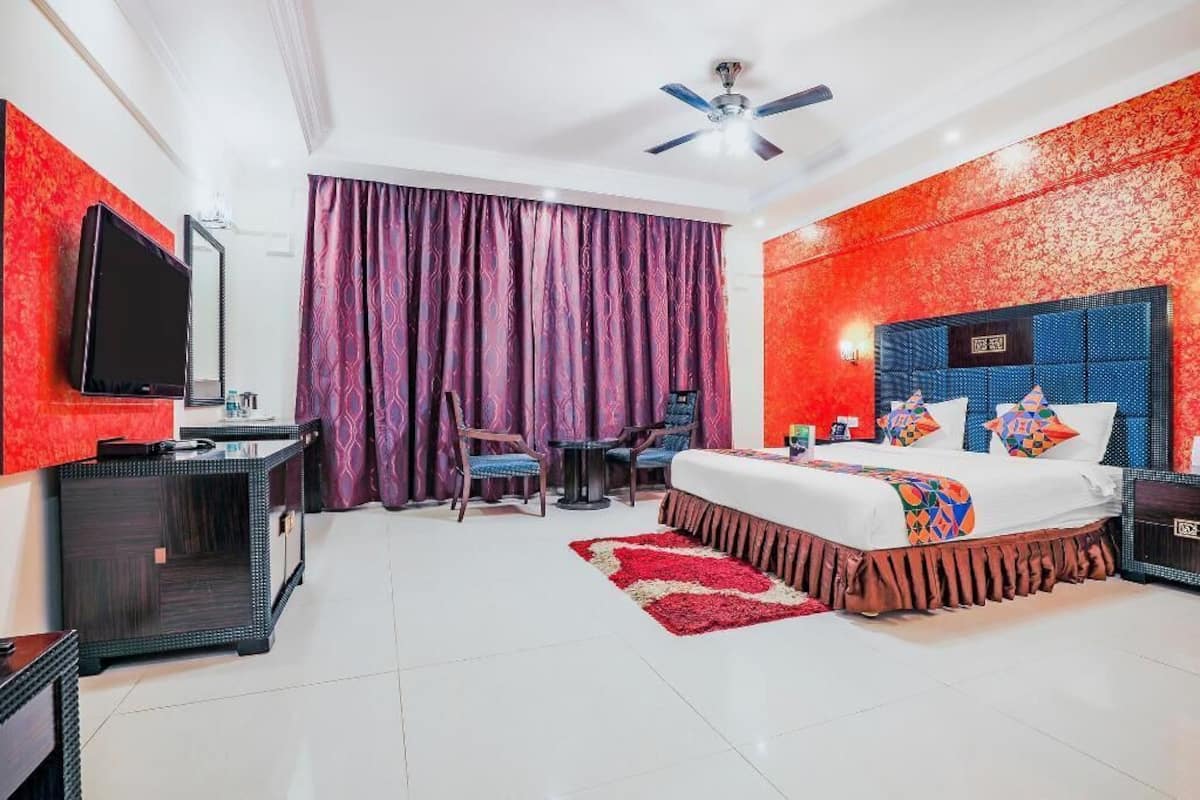 Ein Hotelzimmer mit Bett, Schreibtisch, Stuhl, Fernseher und Deckenventilator.