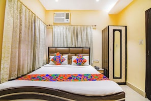 A hotel room with a bed, curtains, an air conditioning unit, a mirror, and a door. - Fabhotel Aayash (Bidhannagar)