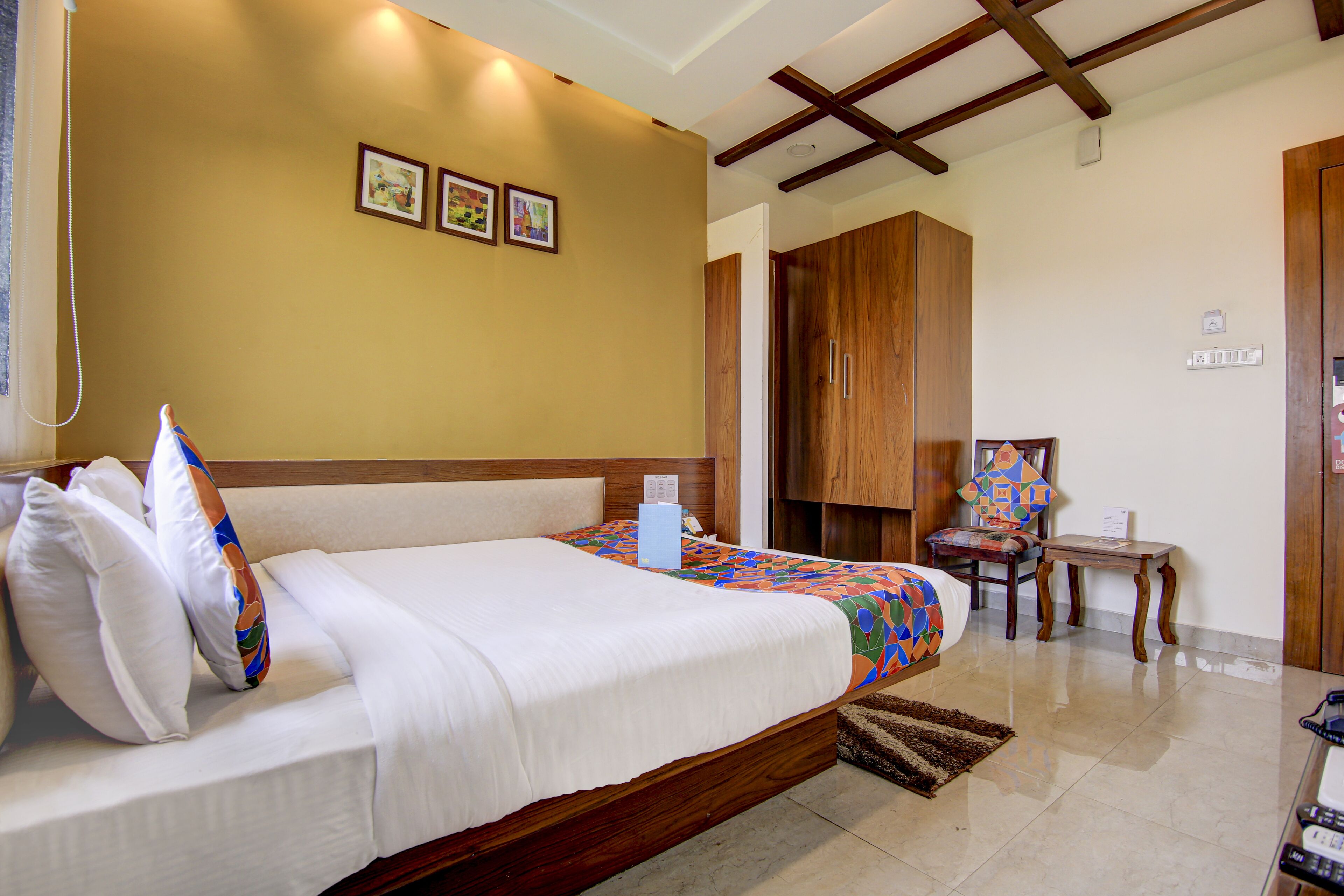 A hotel room with a large bed, wooden wardrobe, and a small table with a chair.