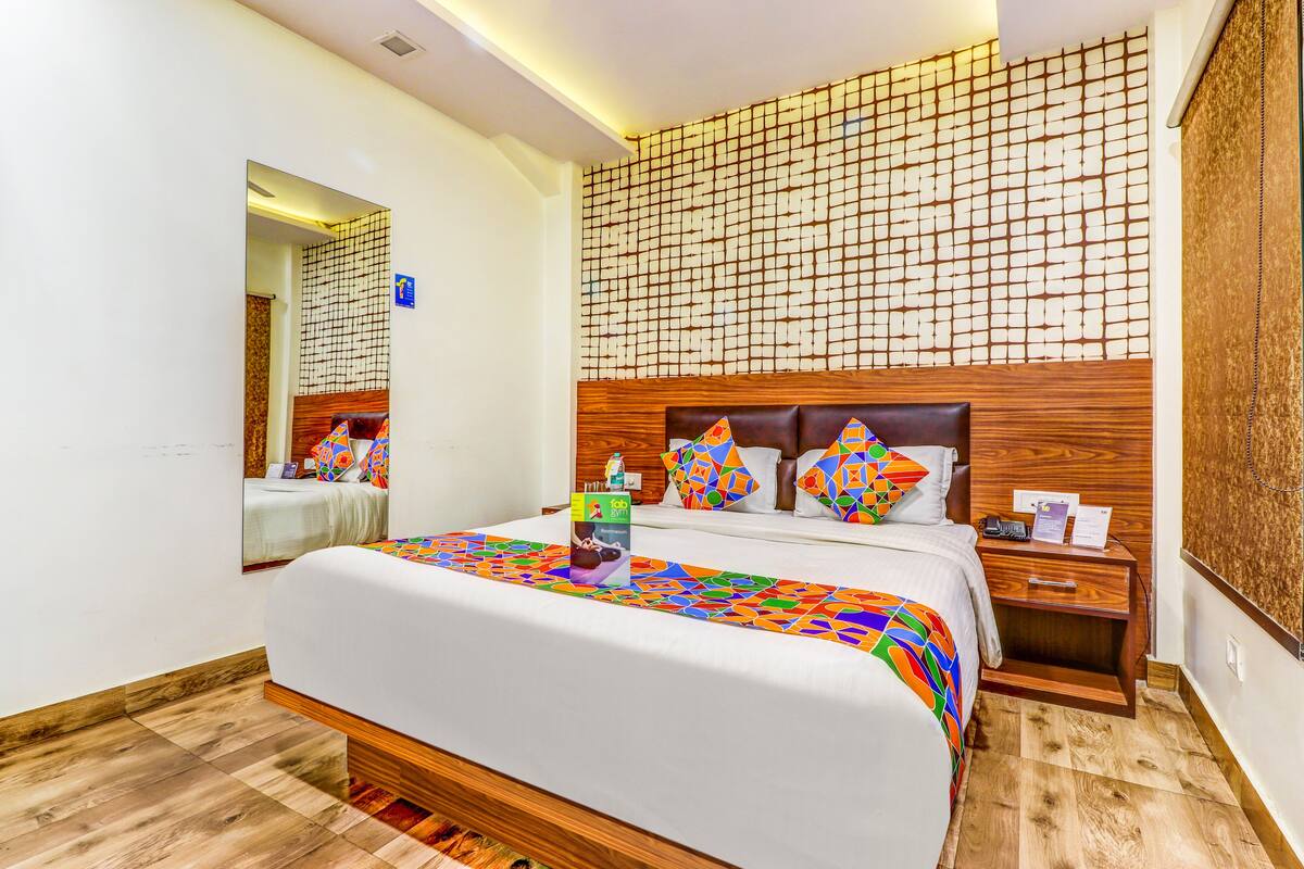 Habitación de hotel con una cama grande, cabecera de madera, mesita de noche y un panel decorativo en la pared.