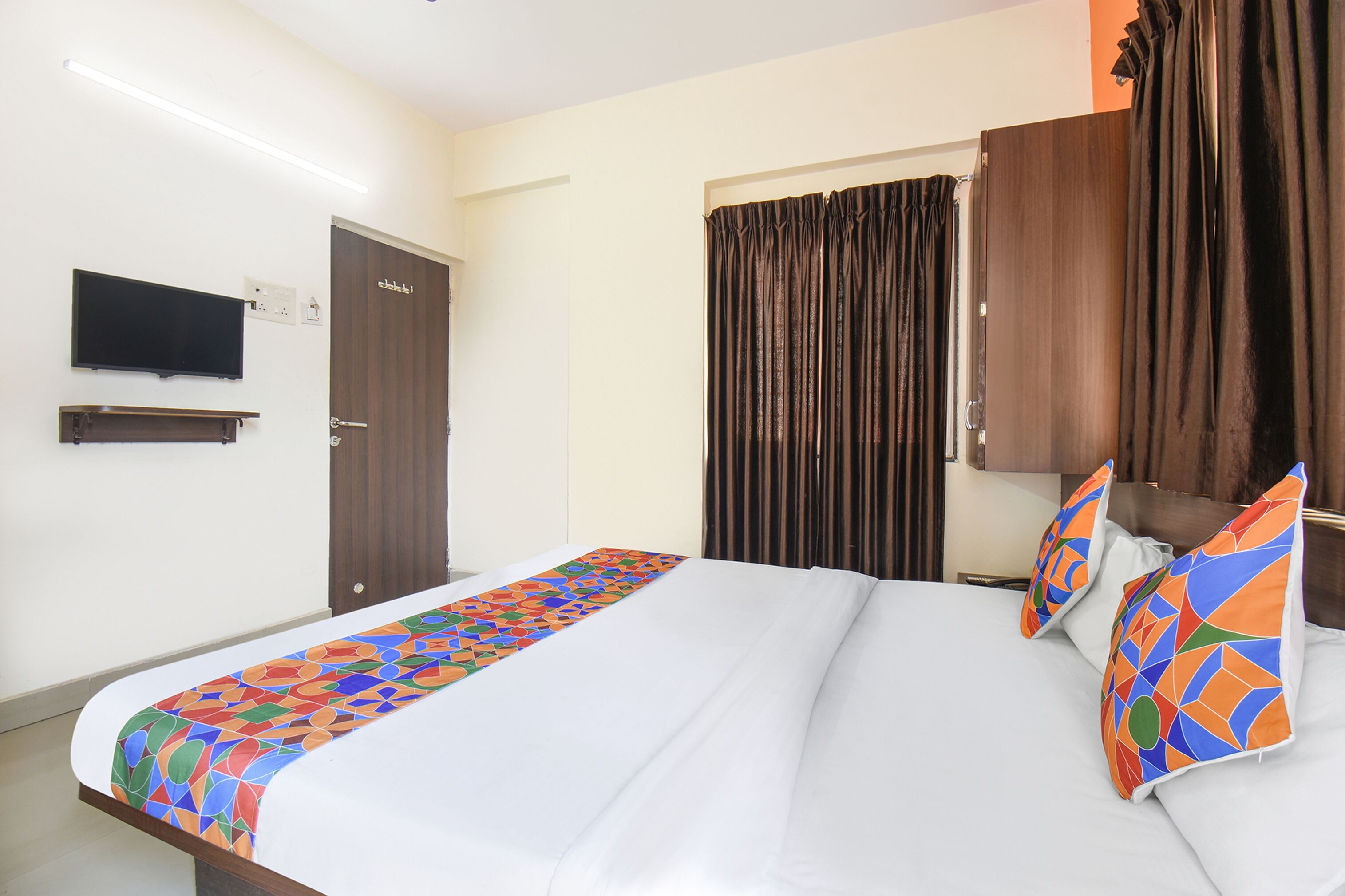 A hotel room with a bed, a television mounted on the wall, and a window with curtains.