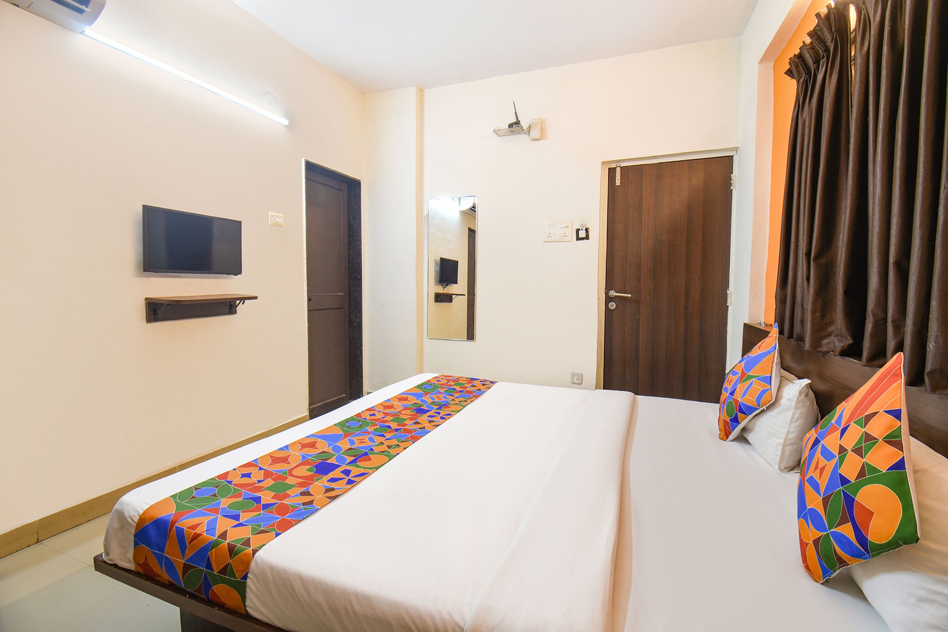 A hotel room with a bed, a television, a mirror, and a door.