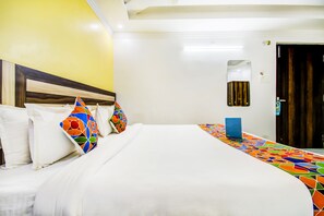 A hotel room with a large bed, white bedding, colorful pillows, a small table, and a wooden door. - Fabhotel Grand Sheela (Patna)