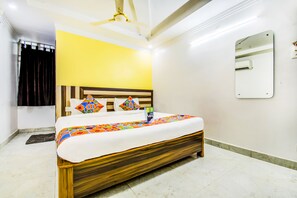 A hotel room with a wooden bed, a yellow wall, a ceiling fan, a mirror, and a window with curtains. - Fabhotel Grand Sheela (Patna)
