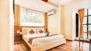 Habitación de hotel con una cama grande, suelo de madera, una ventana con cortinas y una pequeña mesa con una silla.