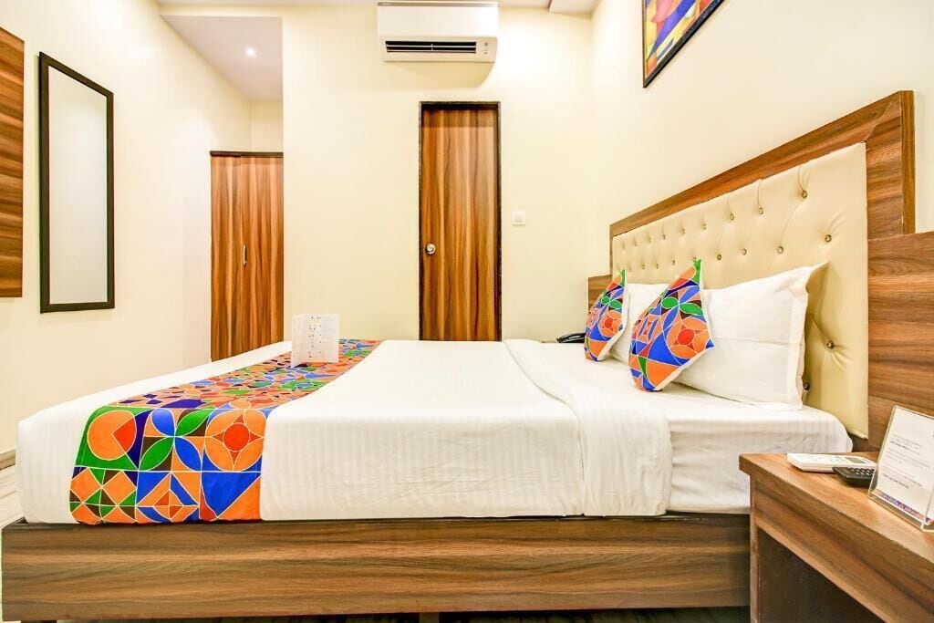 A hotel room with a bed, a wooden headboard, a nightstand, and a wall-mounted air conditioner.
