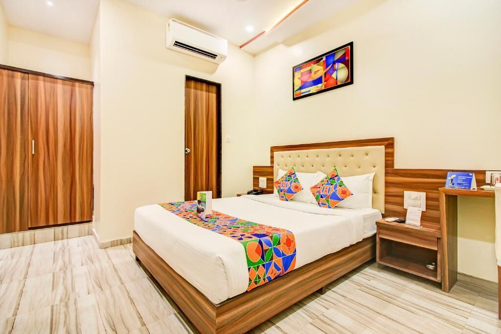 A hotel room with a large bed, wooden wardrobe, and a small bedside table.
