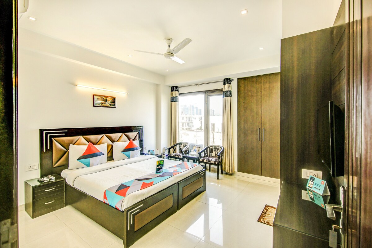 A modern hotel room with a large bed, a ceiling fan, a TV, and a view of the city through the window.