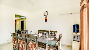 A dining area with a glass table, patterned chairs, a clock, and a water dispenser. - Via Hemkunt Residency - Nr Yatharth Super Speciality Hospital - Noida 110 (Noida)