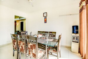 A dining area with a glass table, patterned chairs, a clock, and a water dispenser. - Via Hemkunt Residency - Nr Yatharth Super Speciality Hospital - Noida 110 (Noida)