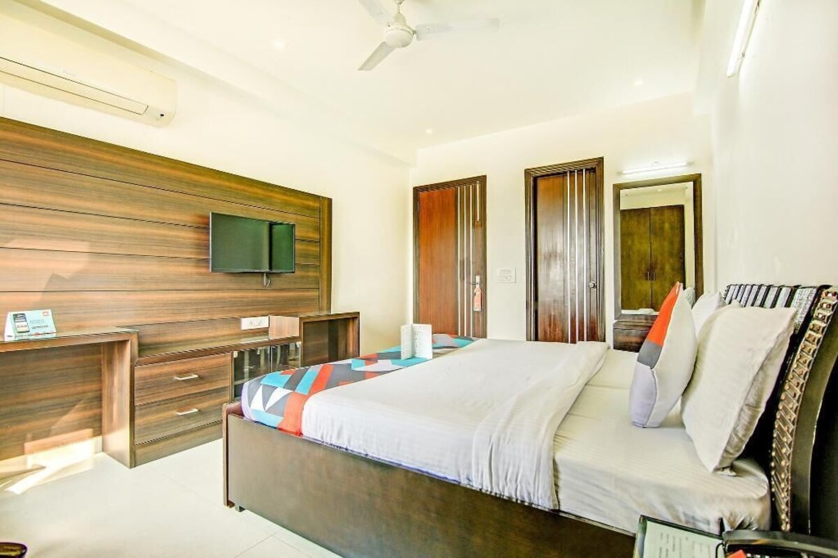 A bedroom with a bed, a TV mounted on a wooden wall, a desk, and a wardrobe.