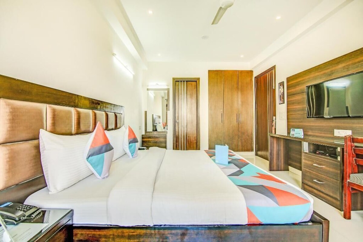 A modern hotel room with a large bed, wooden headboard, a TV, a desk, and a wardrobe.