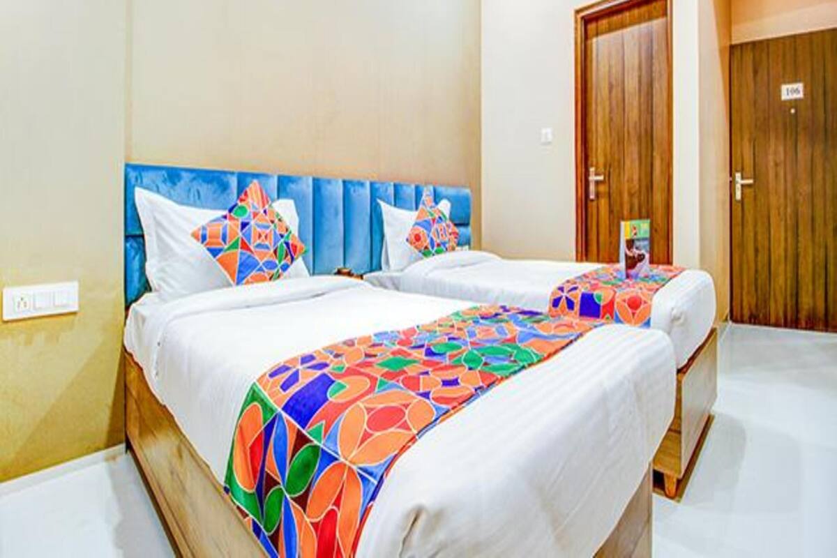 A hotel room with two beds, each with a colorful geometric-patterned bedspread, a wooden headboard, and a wooden door with a number sign.