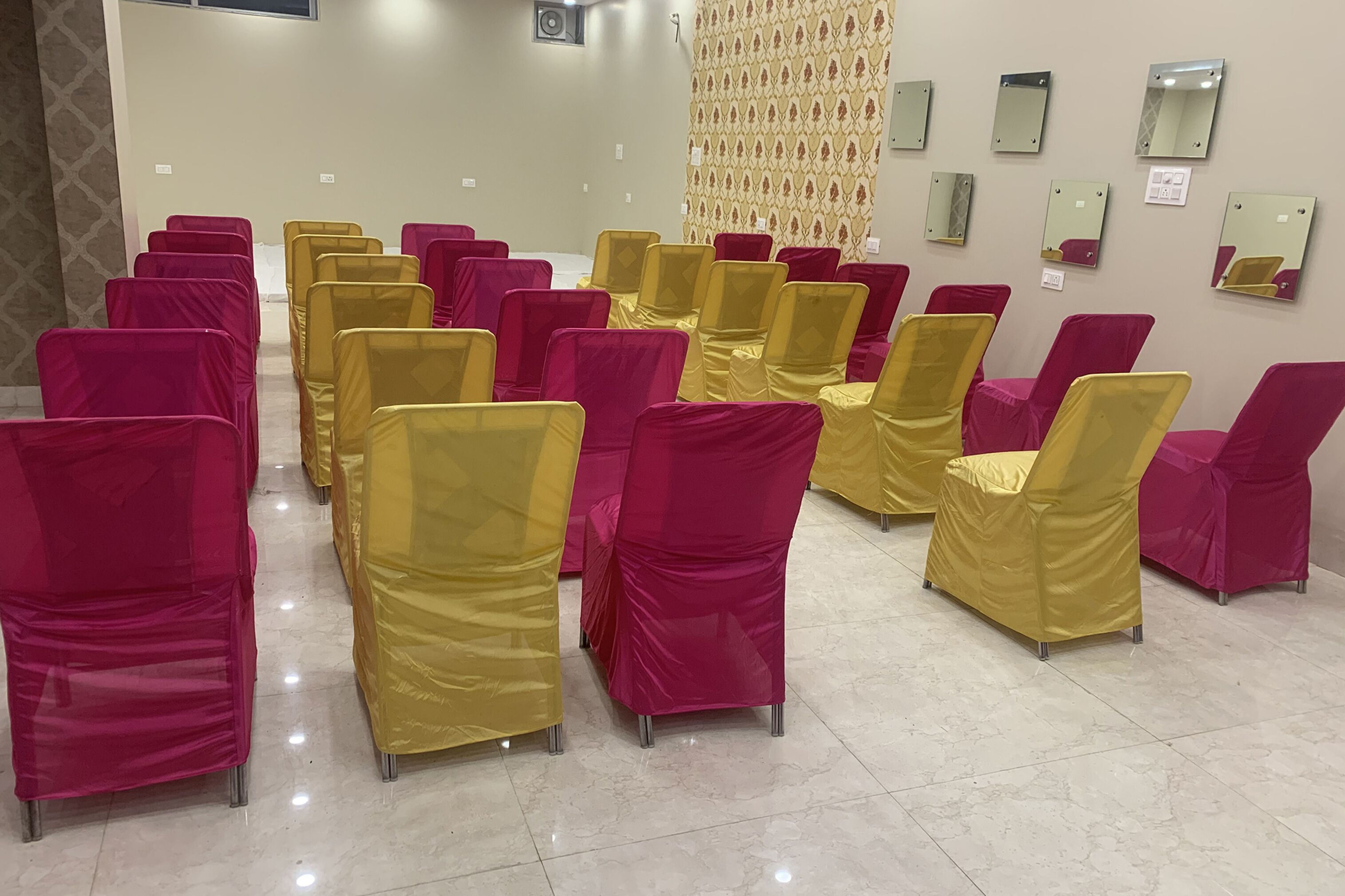 A room with rows of chairs covered in pink and yellow fabric, a patterned wall, and several mirrors.