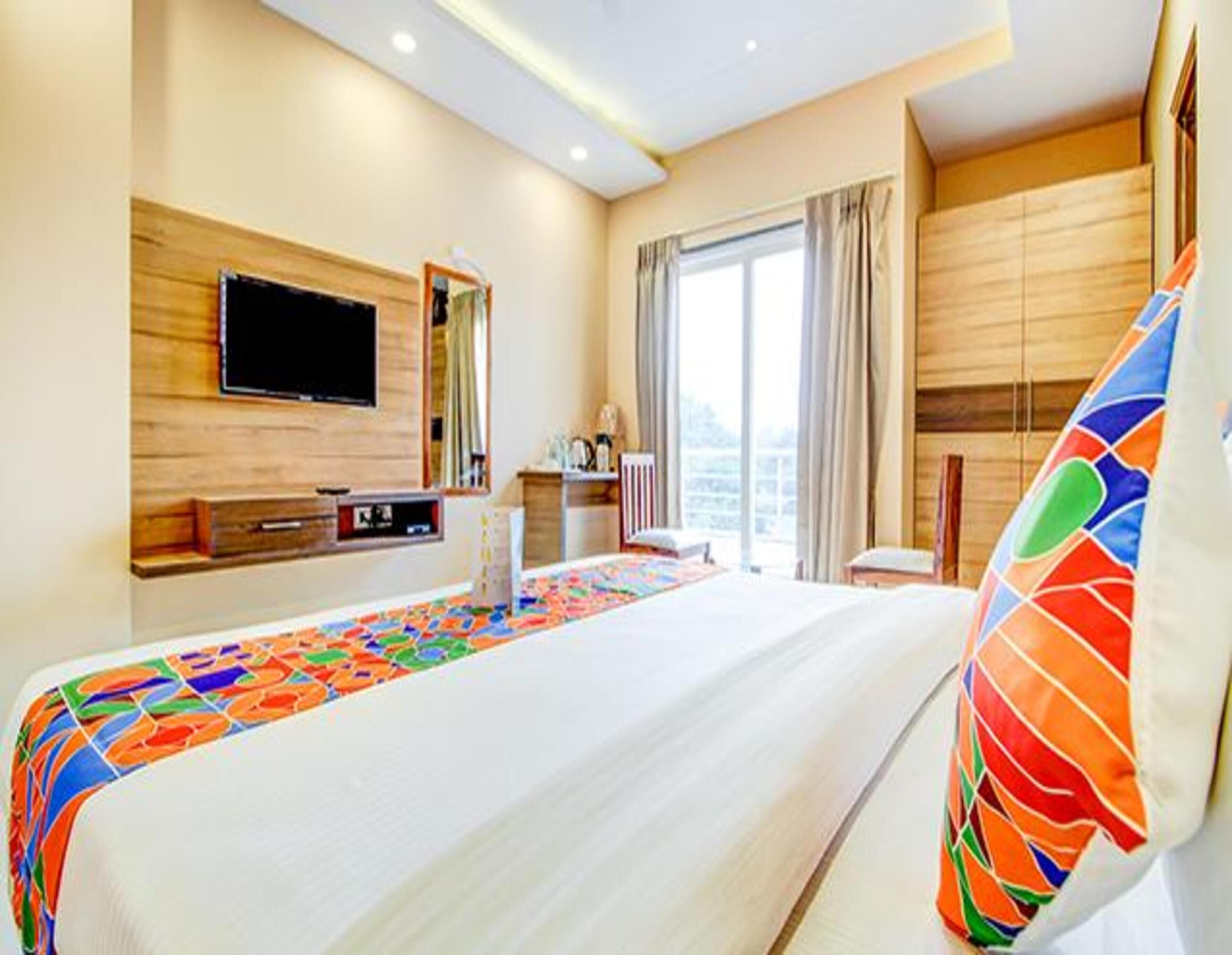 Una habitación de hotel con una cama grande, un televisor de pantalla plana en la pared, un escritorio con una silla y una ventana con cortinas.