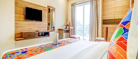 Una habitación de hotel con una cama grande, un televisor de pantalla plana en la pared, un escritorio con una silla y una ventana con cortinas.