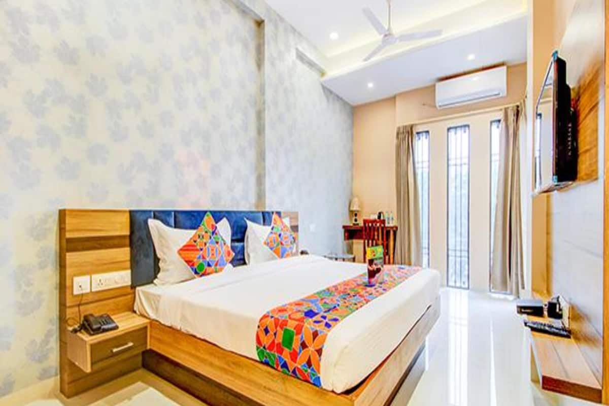 A modern hotel room with a wooden bed, a bedside table with a phone, and a desk with a chair.