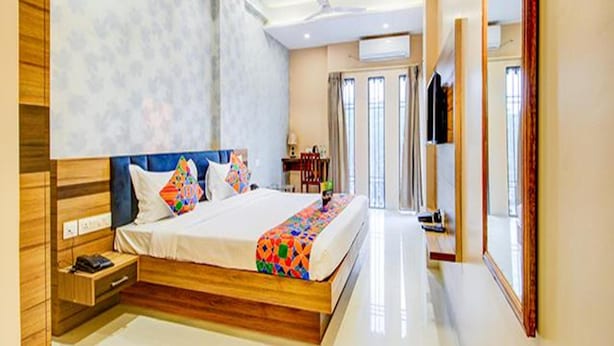 A modern hotel room with a wooden bed, a bedside table, a mirror, and a view of the outdoors. - Fabhotel 7Th Crossing (Jaipur)