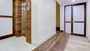 A modern interior with a marble staircase, a wooden accent wall, and a glass door. - Fabhotel Anandam (Raipur)