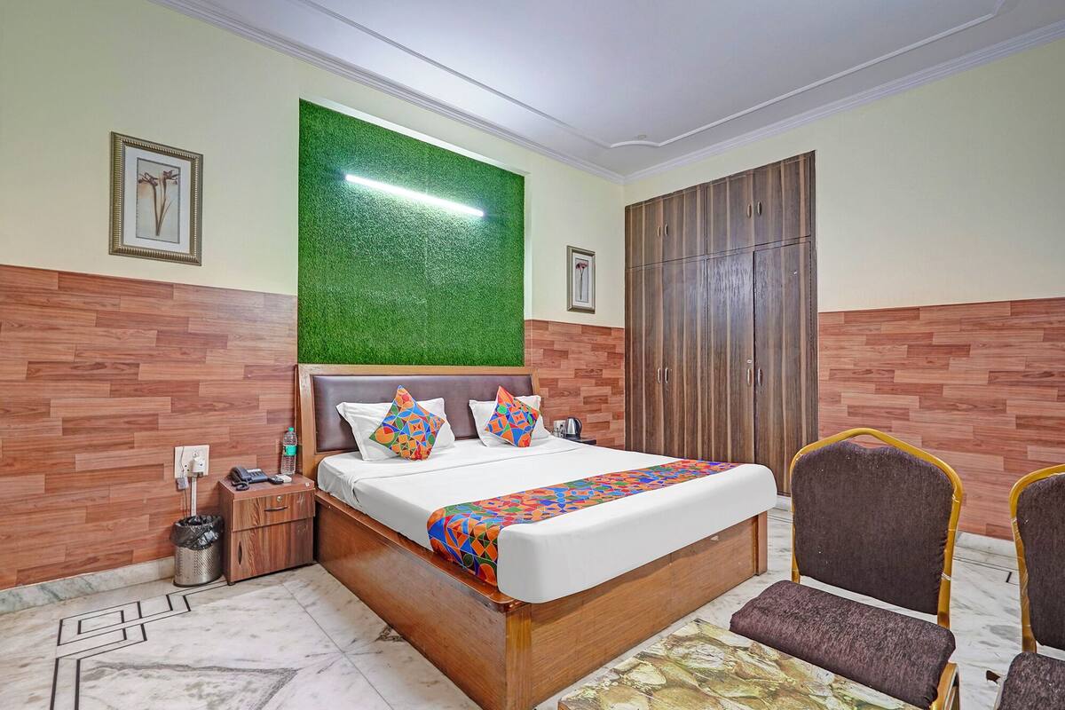 A hotel room with a wooden headboard, a bed with colorful bedding, a green wall, a wardrobe, and a chair.