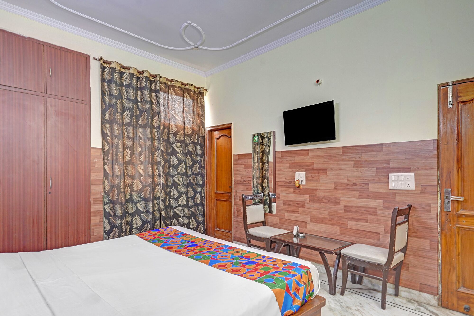 A hotel room with a bed, a desk, a chair, a TV, and a wardrobe.
