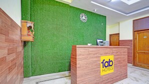 A reception desk with a logo, a green wall with a circular emblem, and a wooden door. - FabHotel The Everest 43 (Noida)