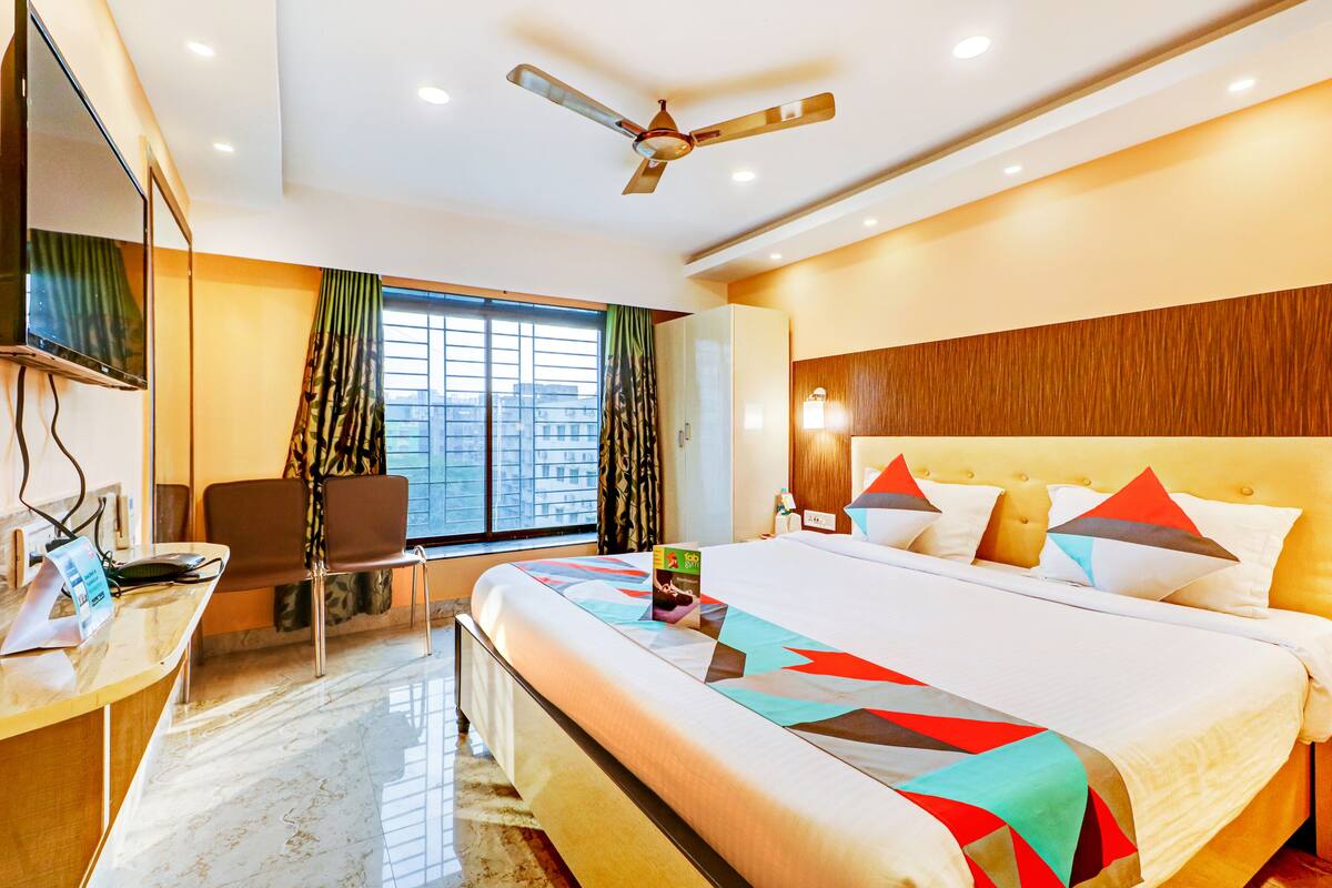 A hotel room with a large bed, a desk with a computer, a chair, a TV, and a window with curtains.